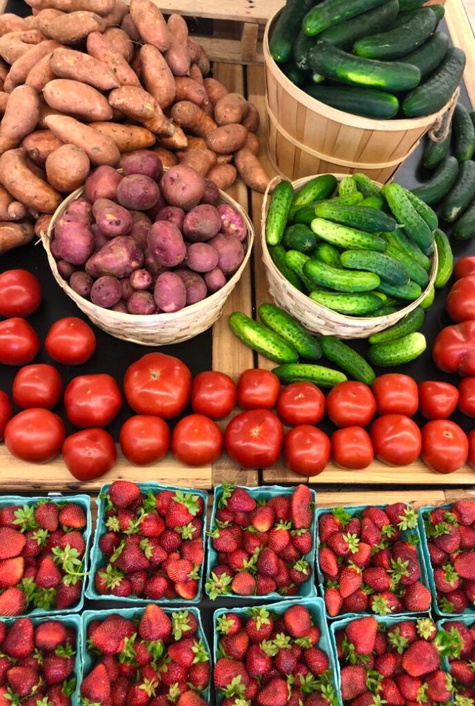 Vibrant display of fresh produce at a farmers market, including potatoes, cucumbers, tomatoes, and strawberries.